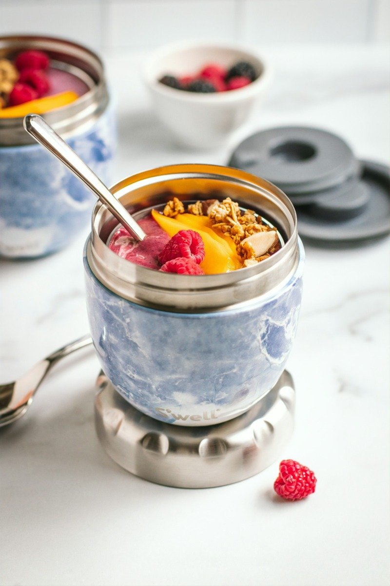 Ein Essensbehälter aus Edelstahl mit Porridge und Beeren, daneben ein Löffel
