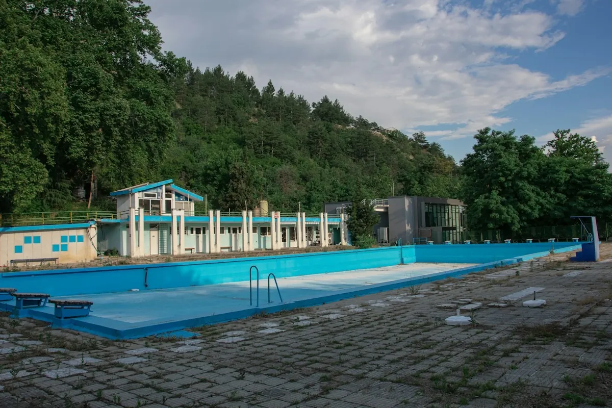 Ein leeres Freibadbecken unter freiem Himmel, dahinter bewaldete Hügel