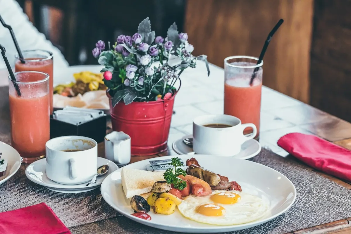 Ein Frühstückstisch mit Spiegeleiern, Kaffeetassen und zwei Gläsern mit rotem Saft