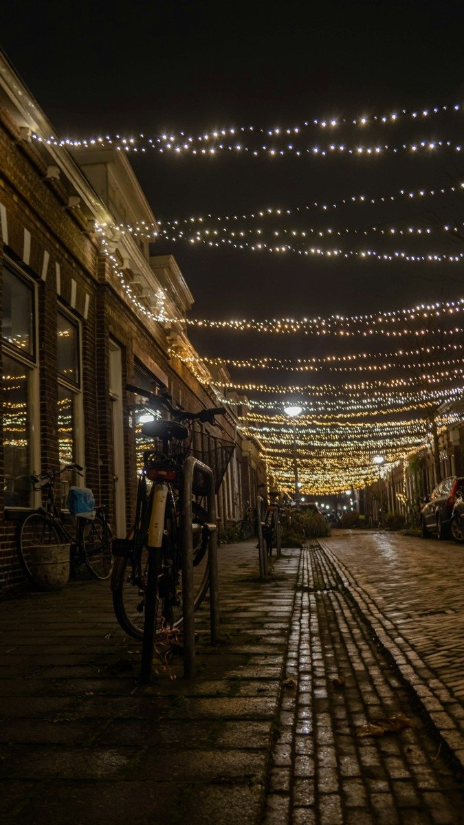Eine schmale Gasse mit Lichterketten über dem Kopfsteinpflaster am Abend
