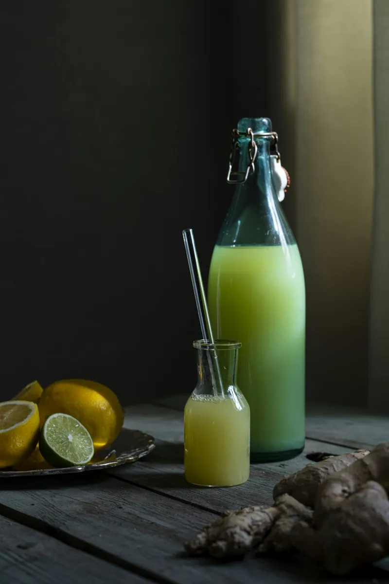 Selbst gemachte Limonade in einer Bügelflasche, daneben Zitronen, Limetten und Ingwer