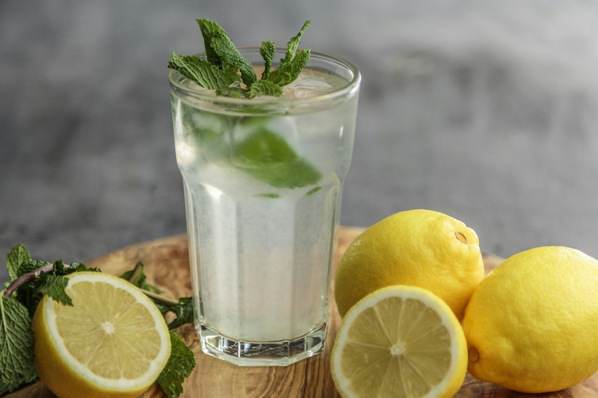 Ein Glas Zitronenlimonade mit Minze, daneben halbierte Zitronen