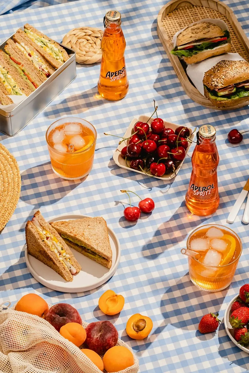 Belegte Brote, Kirschen, Aprikosen und Gläser mit Saft auf einer blau karierten Picknickdecke