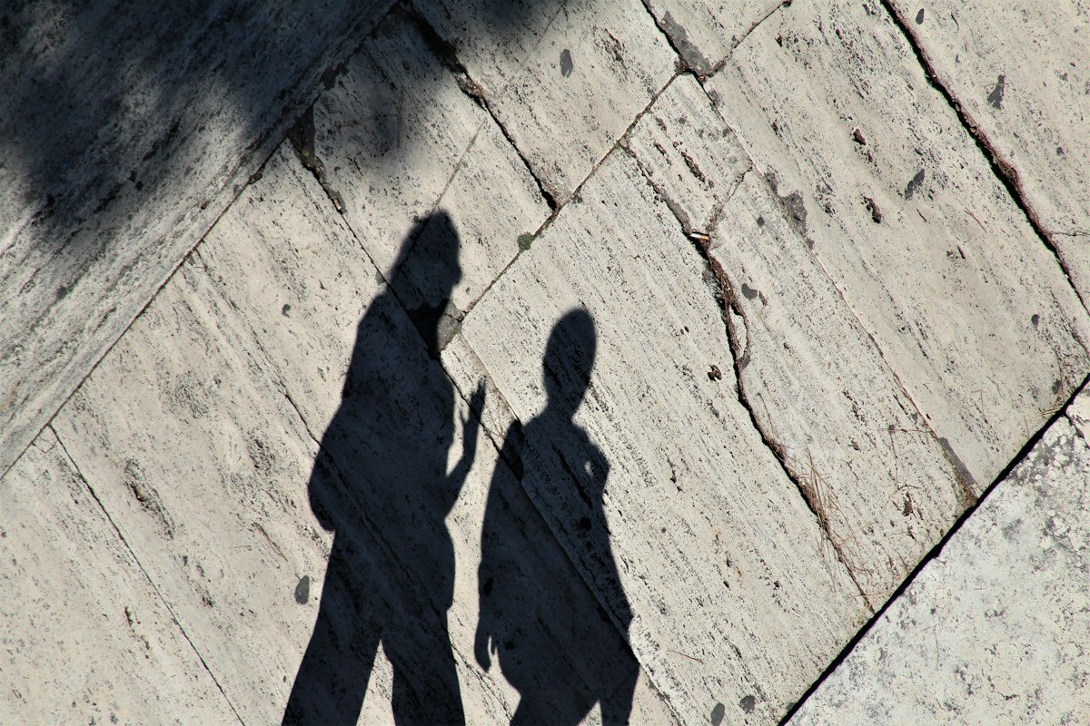 Schatten von zwei Menschen, die nebeneinander über helles Pflaster gehen