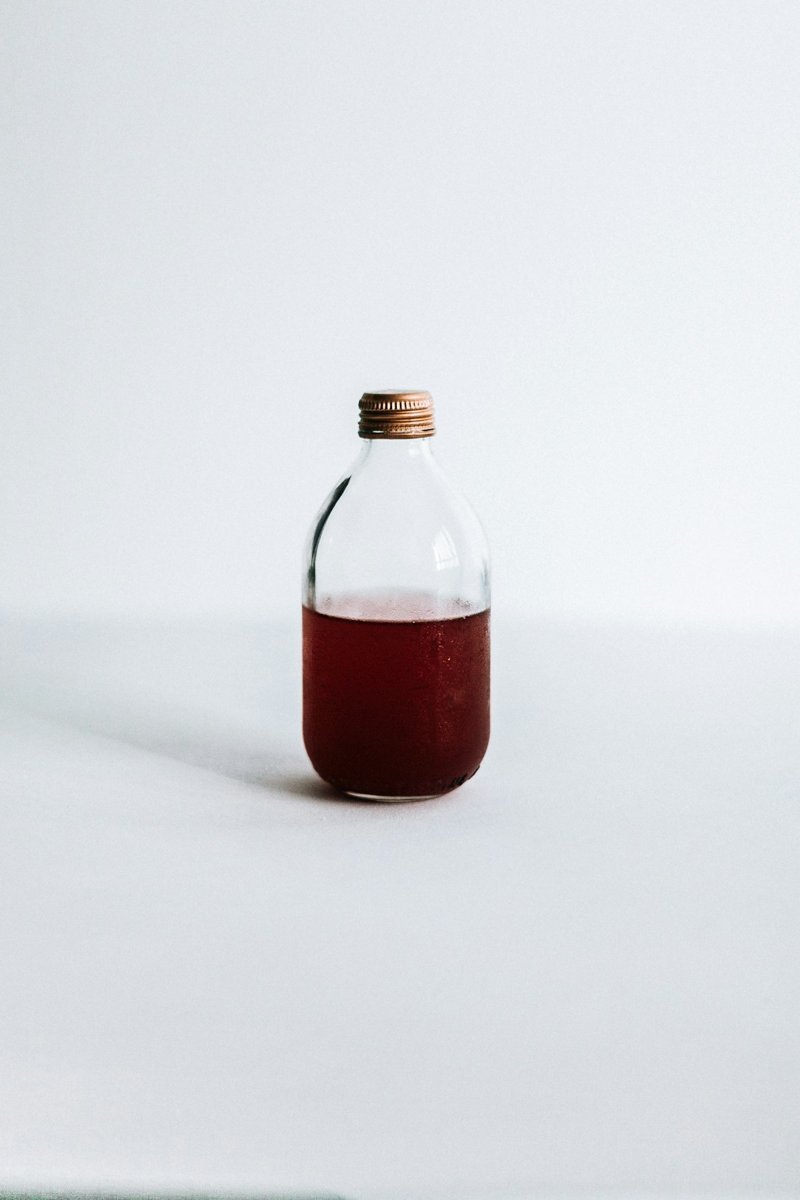 Eine kleine Flasche mit dunkelrotem Sirup auf hellem Grund