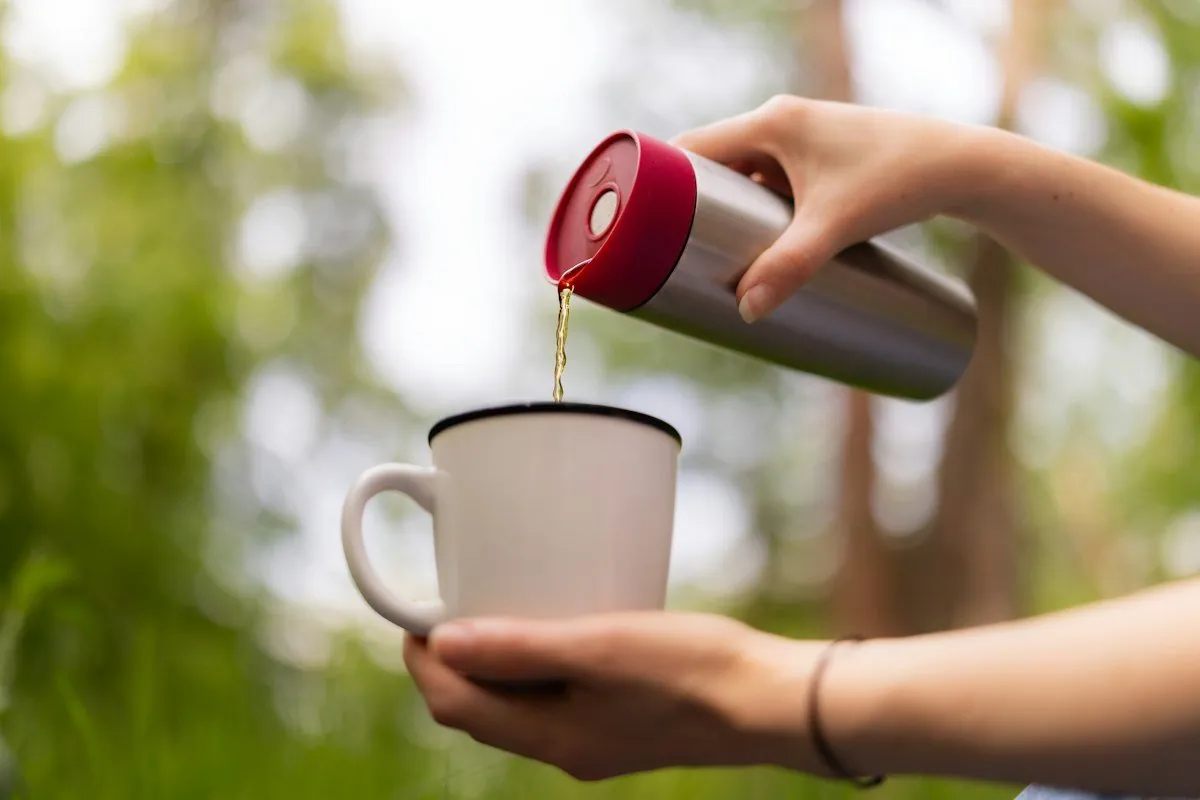 Tee wird aus einer Thermosflasche in eine weiße Tasse gegossen