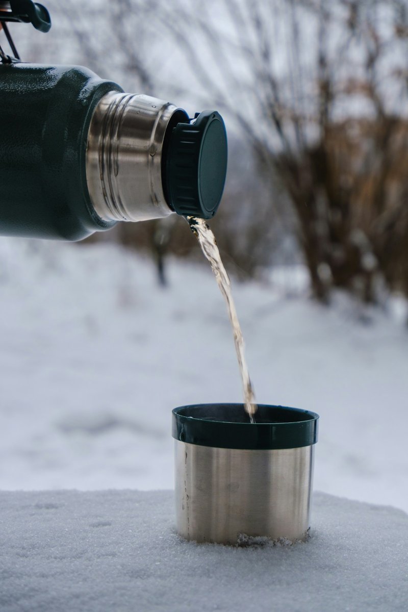 Tee wird aus einer Thermoskanne in einen Becher im Schnee gegossen