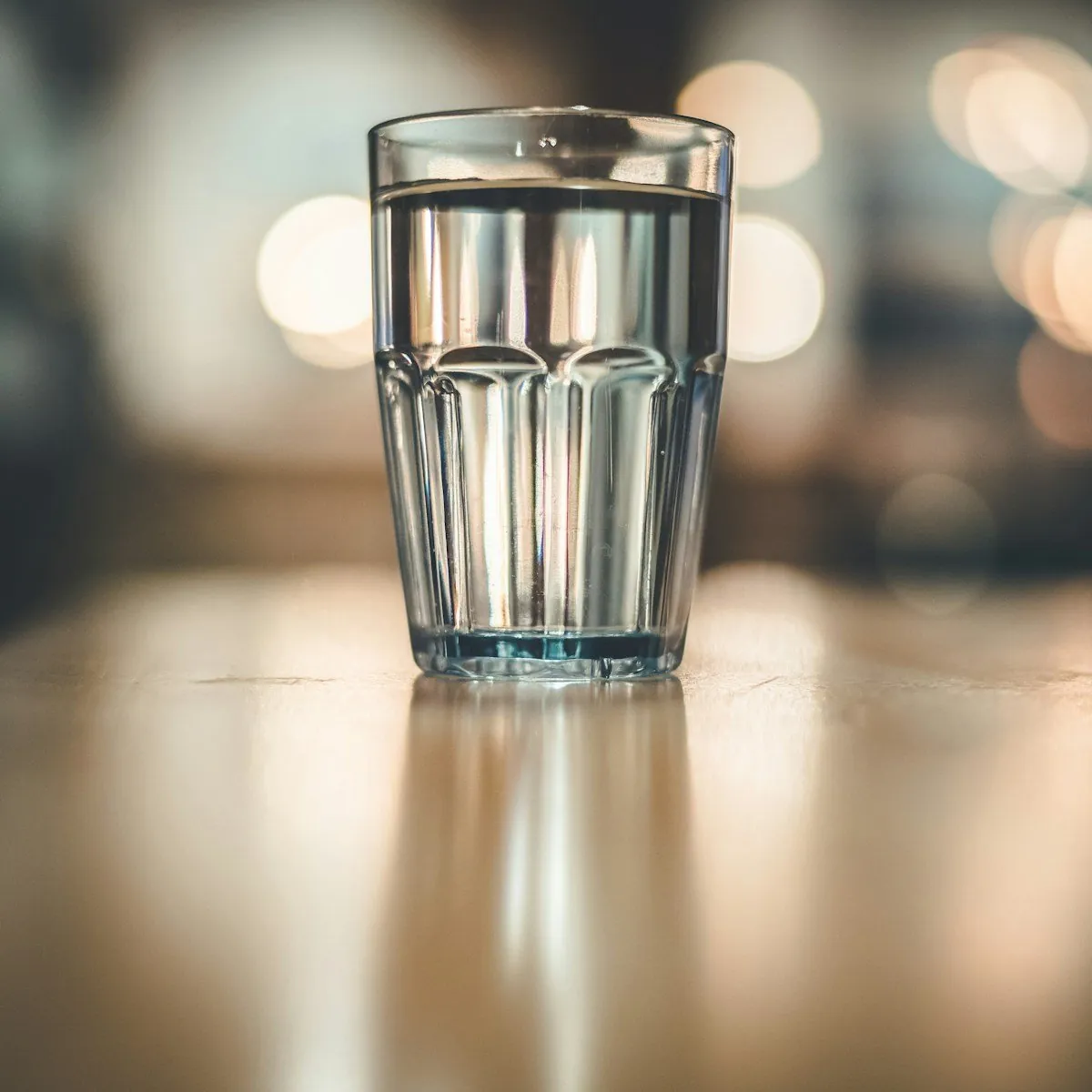 Ein Glas Wasser mit Eis auf einem Tresen, im Hintergrund unscharfe Lichter
