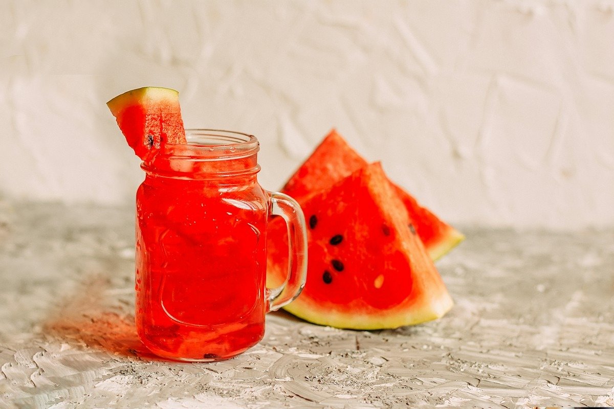 Ein Henkelglas mit rotem Wassermelonengetränk, daneben Melonenstücke
